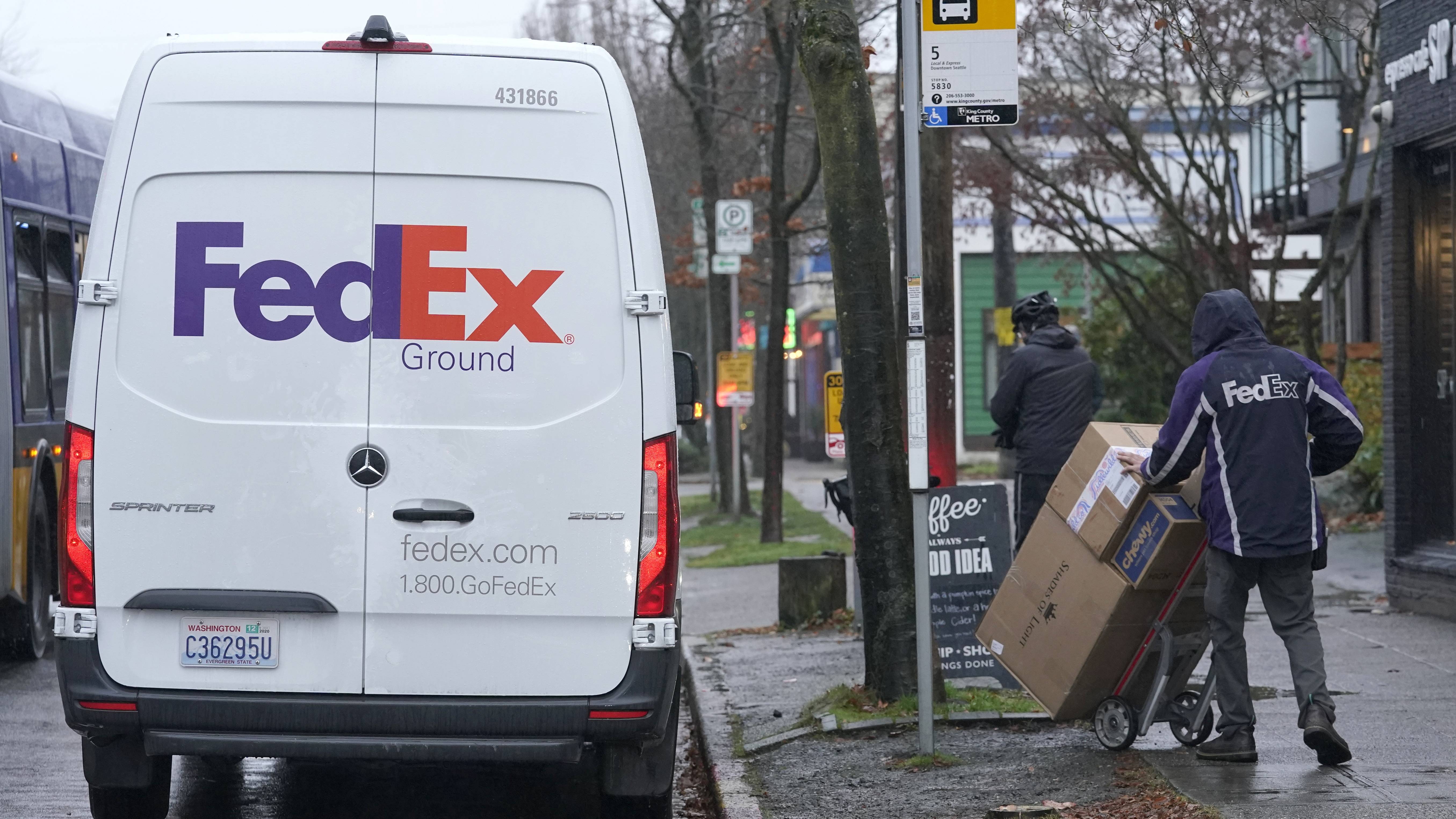 A driver with FedEx carries a package away from a van Tuesday in Seattle. (AP Photo/Ted S. Warren)